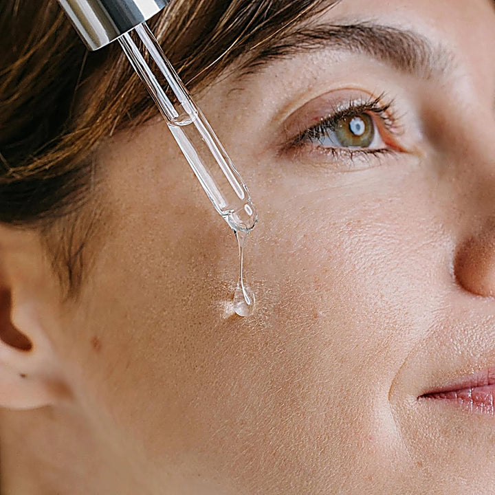 Close-up of a woman's face with a dropper applying a skincare product.