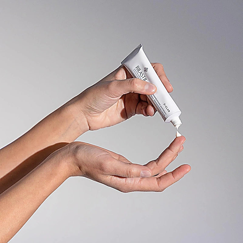 Hand applying white cream from a tube onto another hand against a gray background