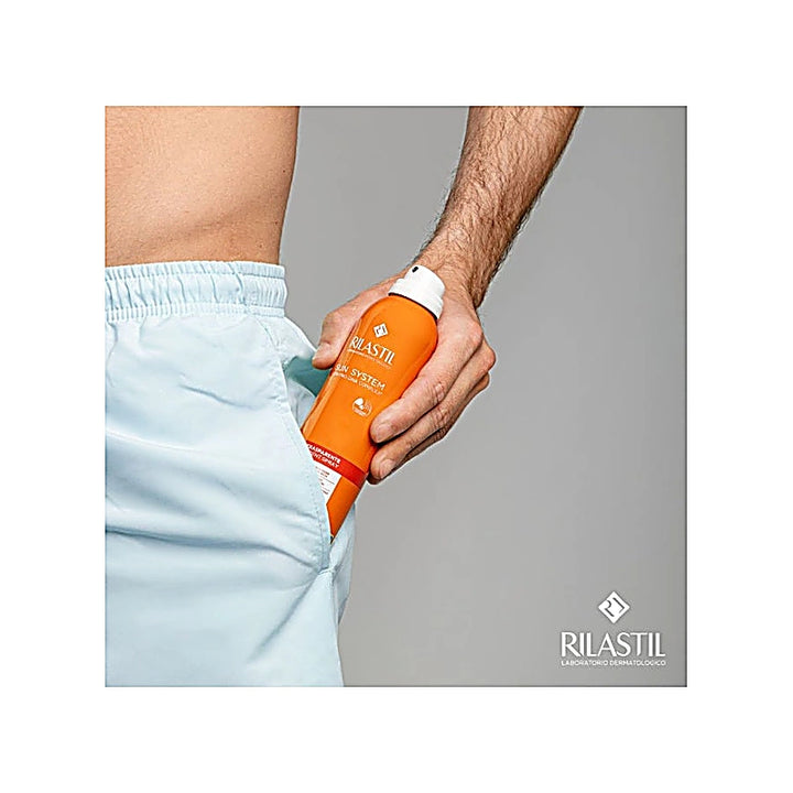 Person holding an orange Rilastil bottle against a gray background