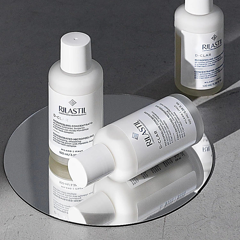 Rilastil skincare bottles on a reflective surface with a dark background