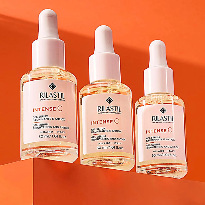 Three bottles of Rilastil Intense C skincare serum on an orange background