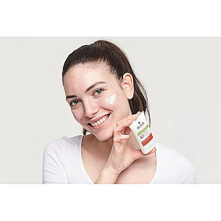 Woman applying sunscreen cream to her face with a white background