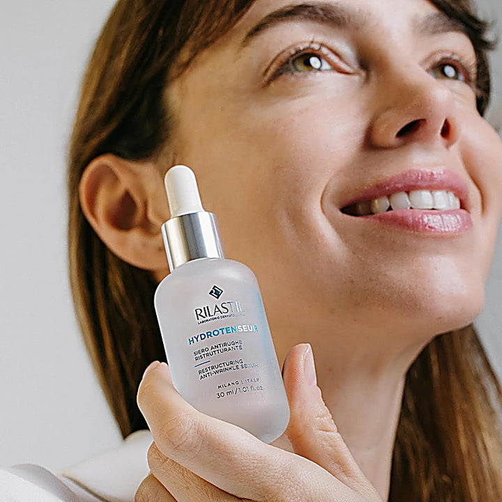 Woman holding a RILAS skincare dropper bottle against a neutral background