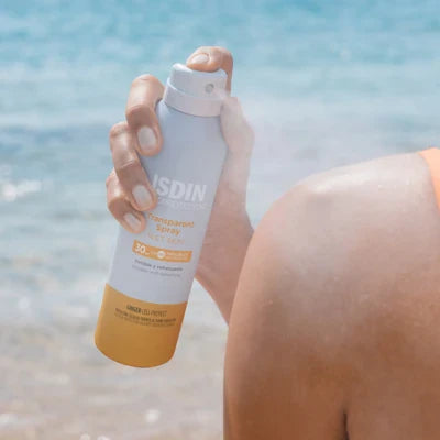 ISDIN Fotoprotector Transparent Spray SPF50 applying on shoulder at the beach, waterproof sunscreen with Ginger Cell Protect and wet skin technology