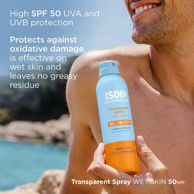 ISDIN Fotoprotector Transparent Spray SPF50 bottle held by a smiling man on the beach with ocean background, showcasing sunscreen for wet skin protection and antioxidant benefits